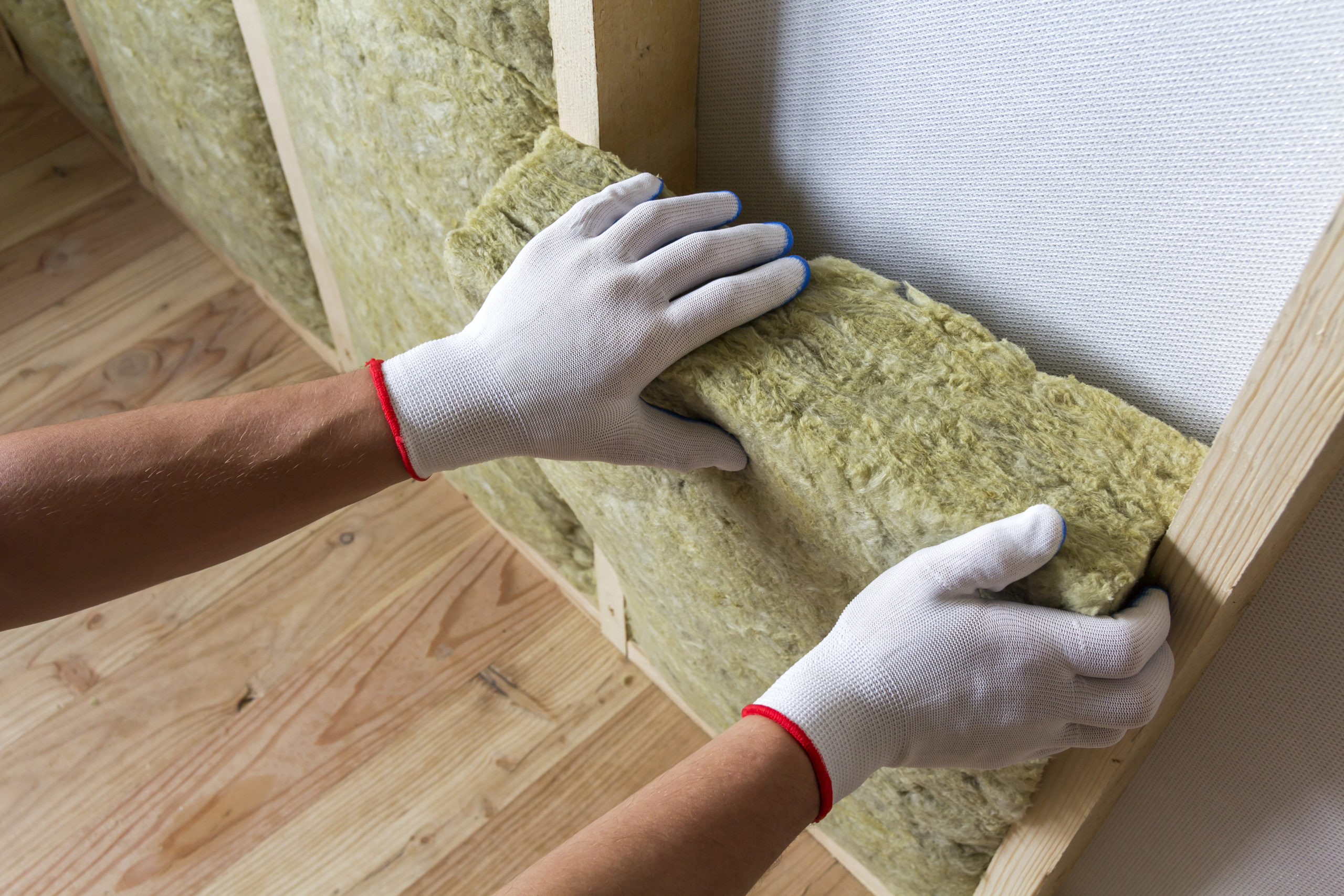 Close-up of worker hands in white gloves insulating rock wool insulation in wooden frame.