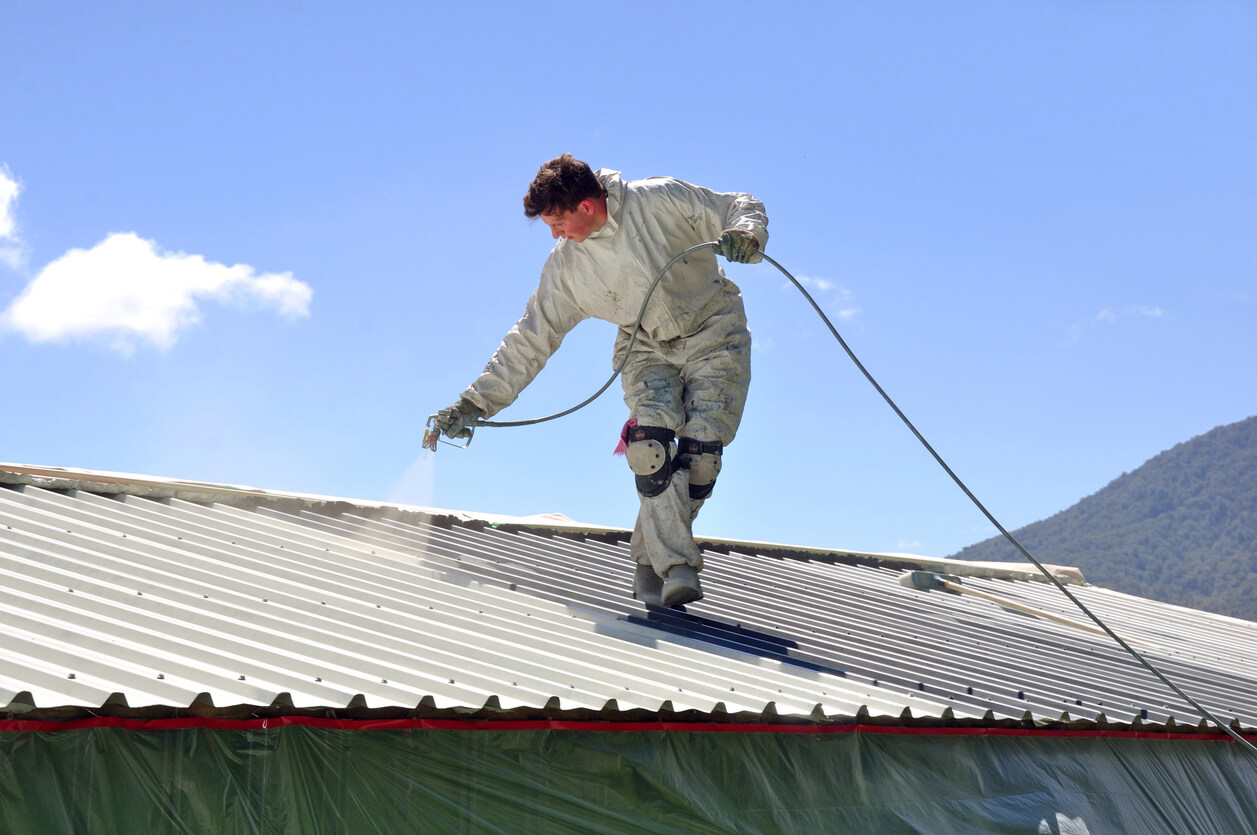 A person painting a roof while wearing a white suit to protect their clothes