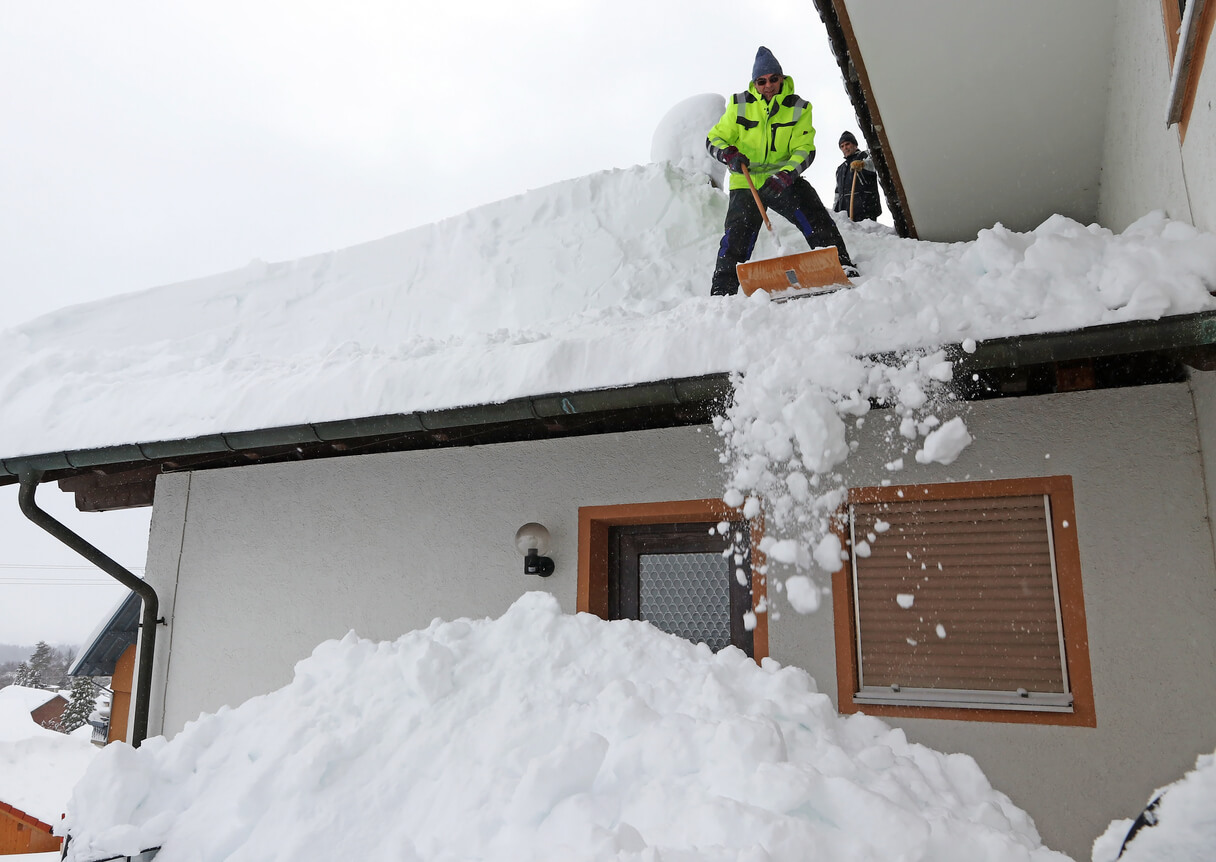 Person shoveling snow off the roof of their home
