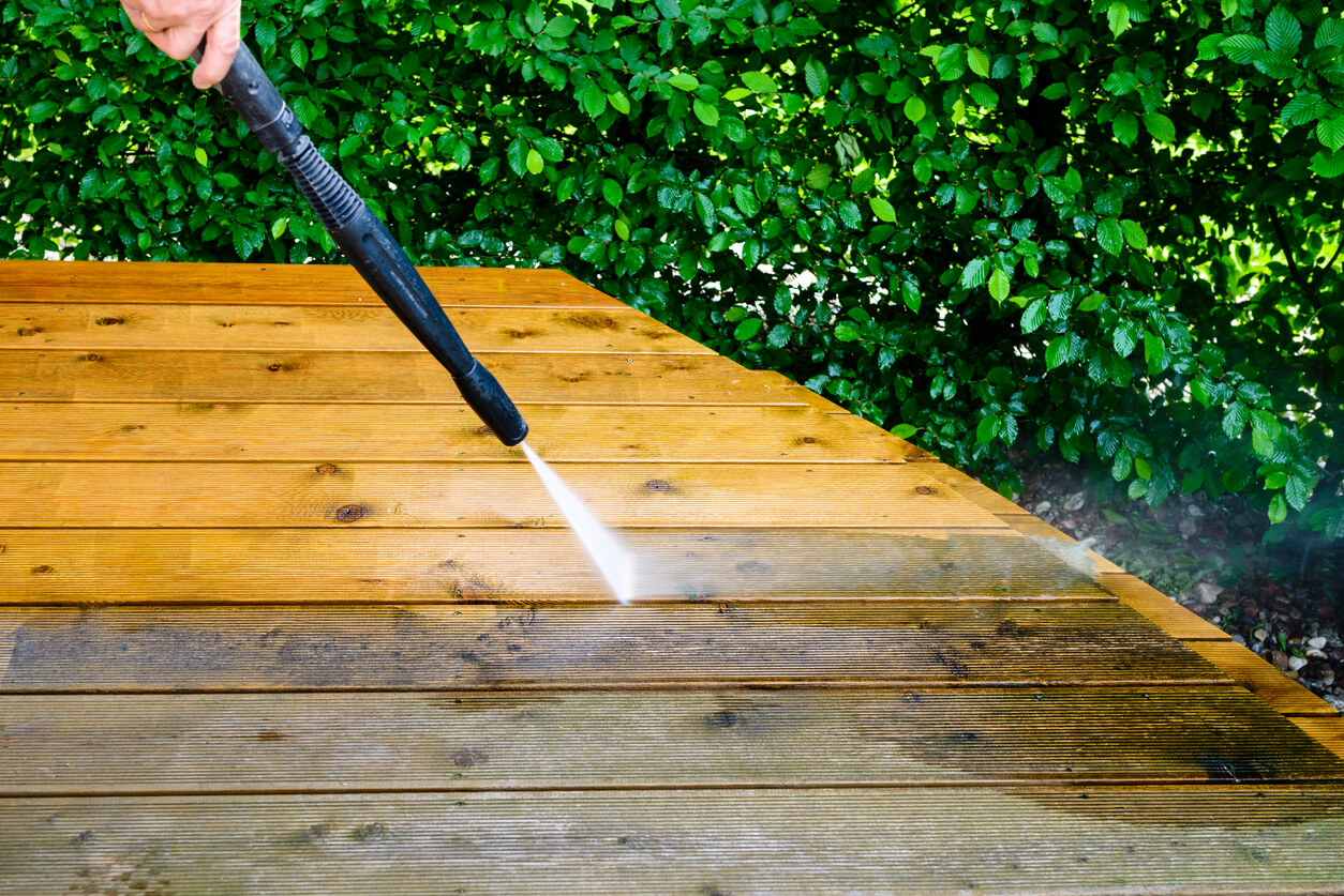 Wood porch being power washed with a stark contrast between the clean wood and dirty, dark wood.