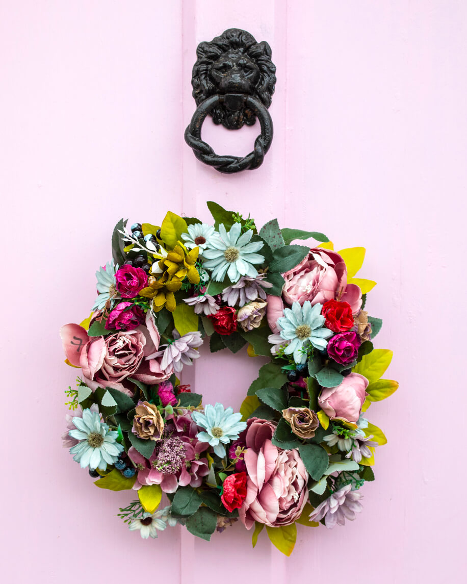 Beautiful pastel wreath with daisies and roses on a pastel pink door with a black lion door knock.