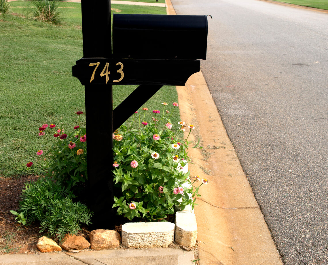 A black mailbox with a small garden at the bottom lined with small stones and bricks