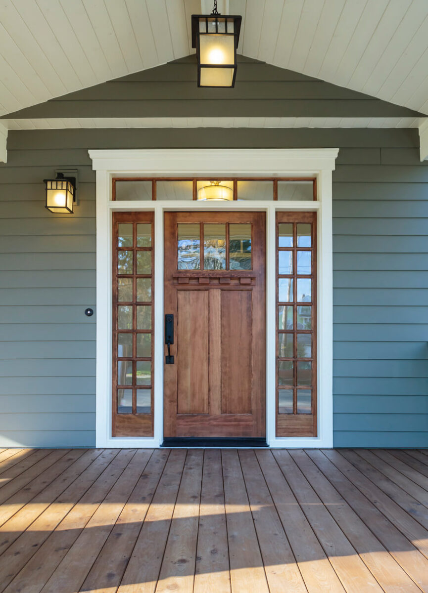 Porched front entrance with medium-colored wood door and trim, new matching square light fixtures at the top of the porch and next to the door.