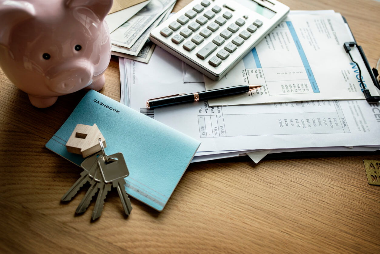 Piggy bank, caculator, and keys laid on a table across some paperwork. Home finance concept.