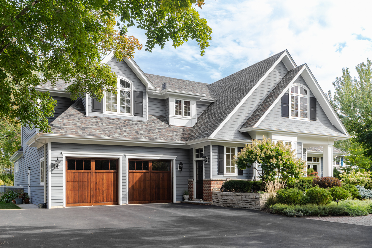 Naperville, IL, USA - A large grey and white modern farmhouse with two wooden garage doors, and beautiful landscaping.
