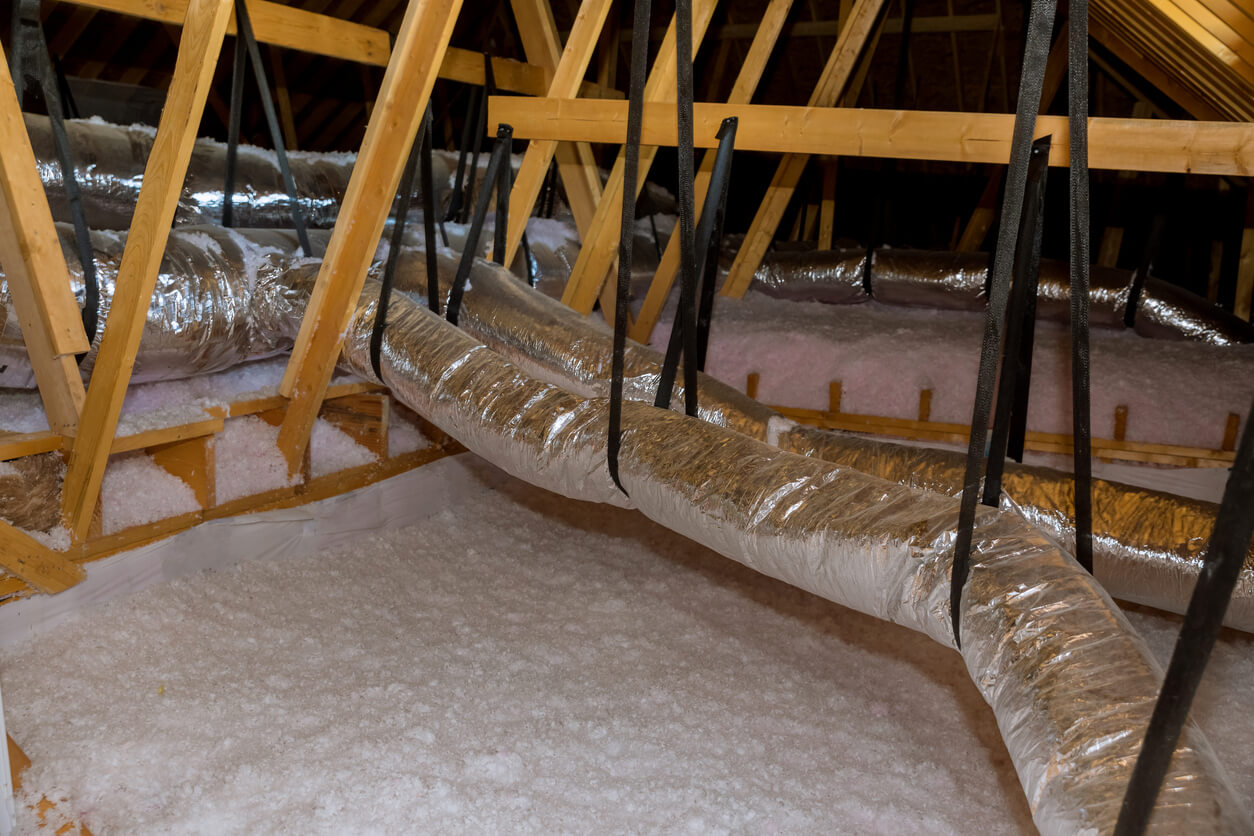 white loose-fill fiberglass insulation being blown into an attic through silver tubes.