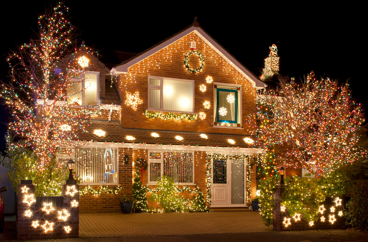 home at night covered in white holiday lights around windows, off of gutters, with wreaths and star shaped lights.