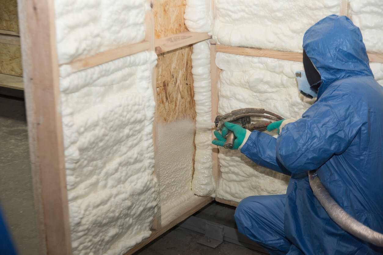 person in blue PPE spraying foam insulation into a wall