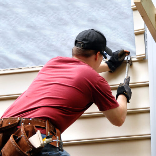 Person in red shirt hammering and installing siding to home