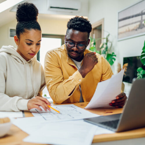 a Black couple reviewing paperwork in front of a laptop and discussing home improvement plans