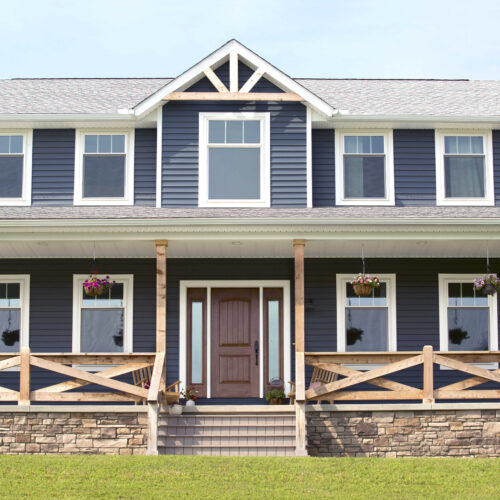 exterior of a large 2 story home with blue siding and rustic wood crossed patio railing