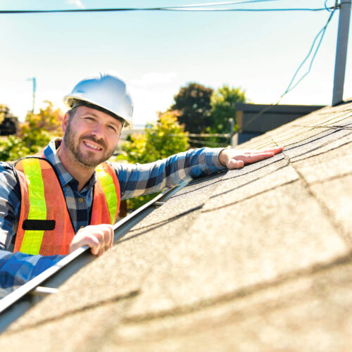 A residential roofing contractor smiling while installing asphalt shingles