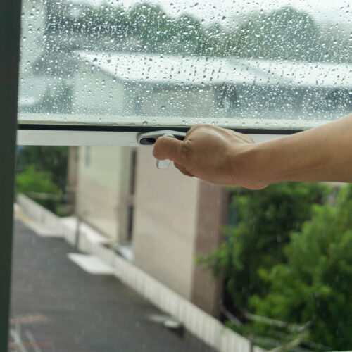 A person opening an awning window on a rainy day.